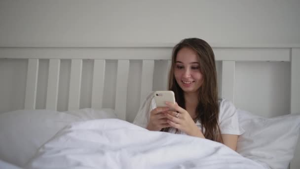 lady is resting in bed and looking at display of smartphone - Filmagem, Vídeo