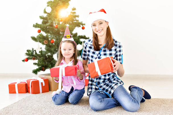Christmas, family and holidays concept - Festive mother and daughter on the couch at home in the living room - 写真・画像