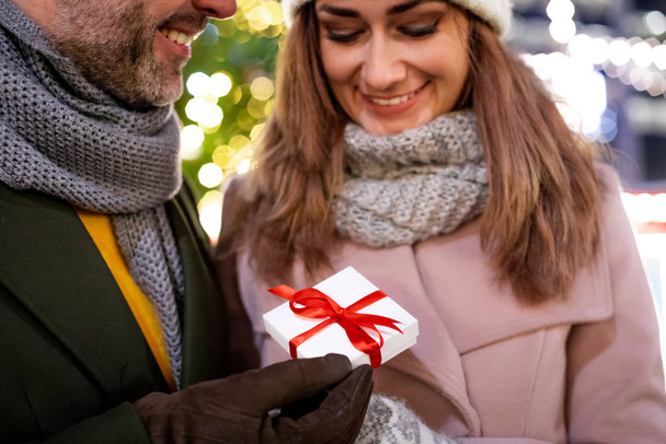 Пара дарит рождественские подарки на фоне наружных украшений во время вечерней прогулки
 - Фото, изображение