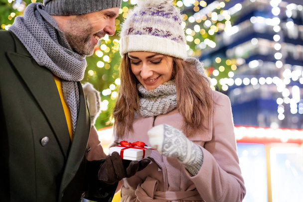 The couple give Christmas gifts against the background of outdoor decorations during an evening walk - Фото, изображение