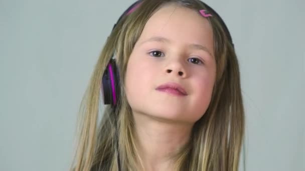 Jolie fille cild souriante écoutant de la musique dans de gros écouteurs roses
. - Séquence, vidéo