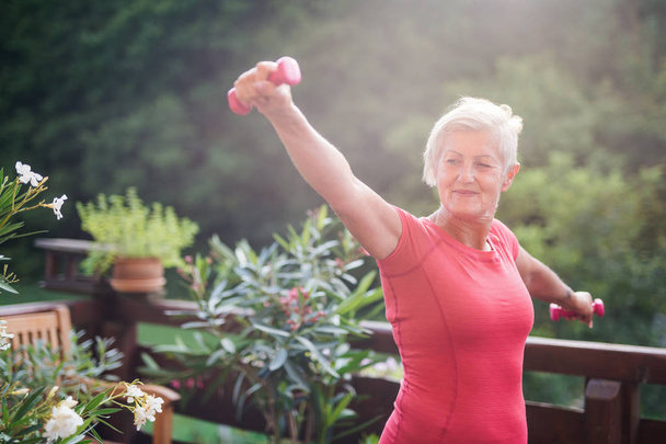 Una donna anziana in piedi all'aperto su una terrazza in estate, facendo esercizio fisico
. - Foto, immagini