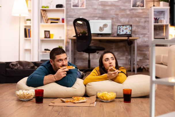 Ζευγάρι κάθεται στο πάτωμα και βλέποντας τηλεόραση στο σαλόνι τους - Φωτογραφία, εικόνα