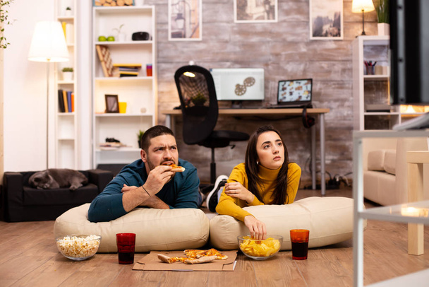 Couple sitting on the floor and watching TV in their living room - Foto, Imagen