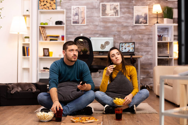 Pár sedí na podlaze a dívají se na televizi v obýváku - Fotografie, Obrázek