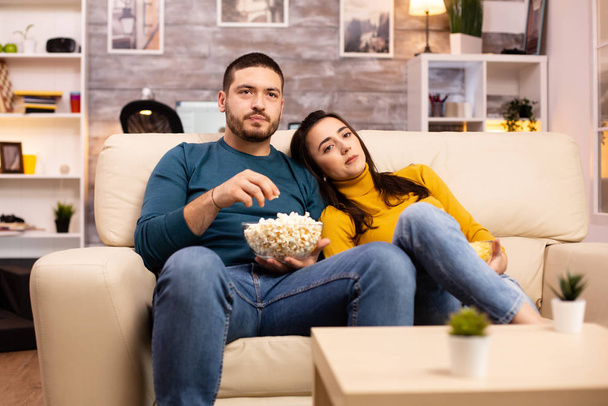 Jóképű pár otthon popcornt eszik és TV-t néz. - Fotó, kép
