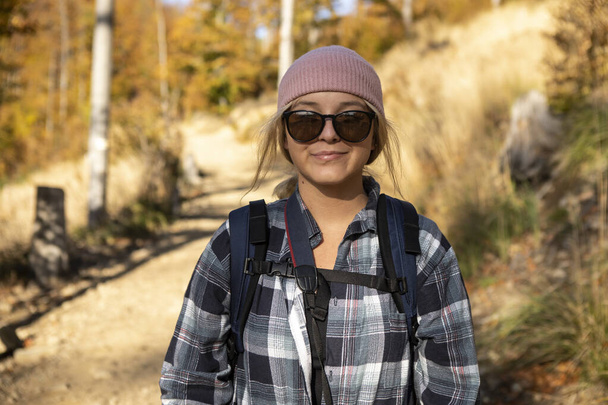 uśmiechnięta kobieta w czapce z plecakiem wędrująca po górach - Zdjęcie, obraz