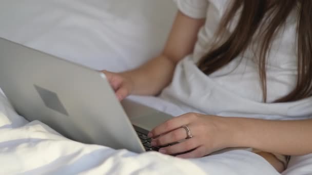 woman is typing text on laptop sitting in bed, closeup - Video
