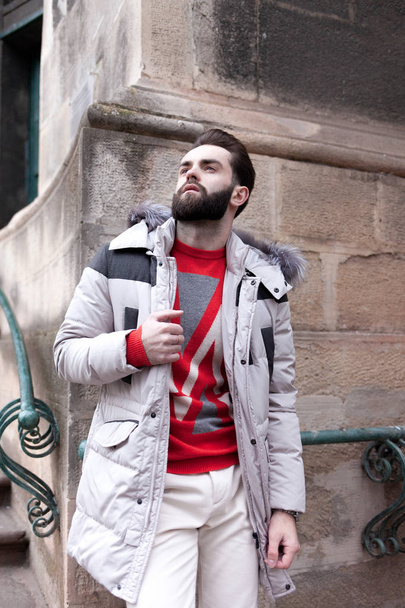 Charmant homme élégant avec une barbe dans une veste d'hiver avec de la fourrure posant à l'extérieur. Portrait d'un gars élégant en beaux vêtements
 - Photo, image