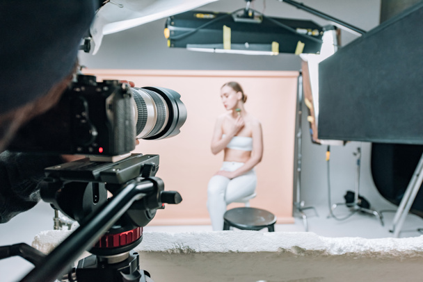 Επιλεκτική εστίαση του videographer με κάμερα και μοντέλο στο φωτογραφικό στούντιο με προβολείς - Φωτογραφία, εικόνα