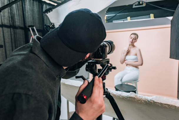 Vista trasera del videógrafo filmando modelo atractivo con rodillo de masaje bajo focos
 - Foto, Imagen
