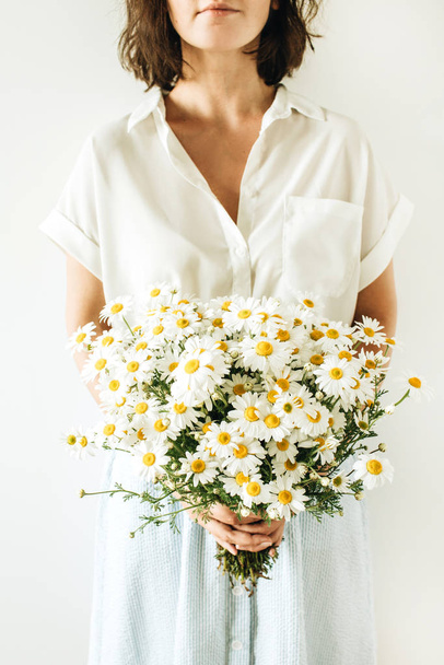 Young woman hold in hands bouquet of white chamomile daisy flowers on white background. - Фото, изображение