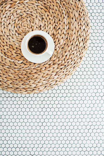 Flat lay cup of coffee on rattan straw puff on white mosaic tile. Morning breakfast. Minimal modern interior design concept. Top view. - Фото, изображение