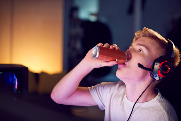 Teenage Boy Drinking Caffeine Energy Drink Gaming At Home Using Dual Computer Screens At Night - Foto, immagini