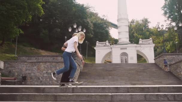 Ten chlap učí svou přítelkyni jezdit na skateboardu. Datum hipsterů. - Záběry, video