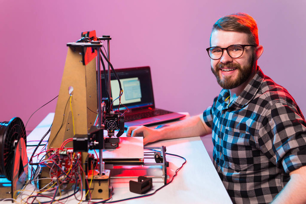 Jonge mannelijke ontwerper die in het laboratorium een 3D-printer gebruikt en een prototype, technologie en innovatieconcept van een product bestudeert - Foto, afbeelding