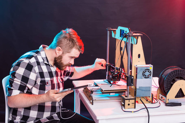 Νεαρός σχεδιαστής αρσενικού μηχανικού που χρησιμοποιεί τρισδιάστατο εκτυπωτή στο εργαστήριο και μελετά ένα πρωτότυπο προϊόν, την τεχνολογία και την καινοτομία - Φωτογραφία, εικόνα