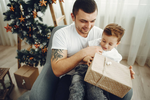 Cheerful father and son sitting near Christmas decorations. The boy is sitting with joy - Zdjęcie, obraz