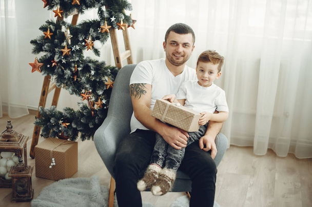 Cheerful father and son sitting near Christmas decorations. The boy is sitting with joy - Фото, зображення