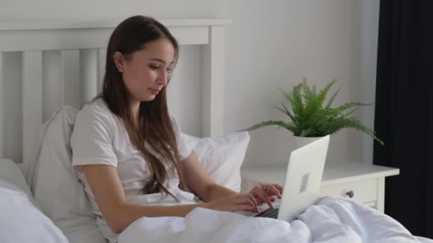 woman is resting in bed and typing messages on laptop in morning - Video, Çekim
