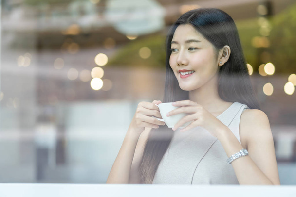 Asijská mladá žena držící šálek kávy v moderní kavárně nebo coworking prostor vedle okna zrcadlo, japonky, čínsky, korejský životní styl a každodenní život, podnikatelský koncept - Fotografie, Obrázek