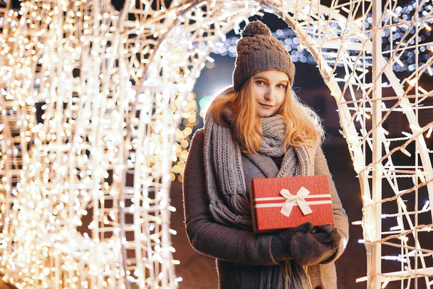 Dívka držící dárkovou krabici na zimním festivalu. Šťastná žena s vánoční dárek přes vánoční pozadí. - Fotografie, Obrázek