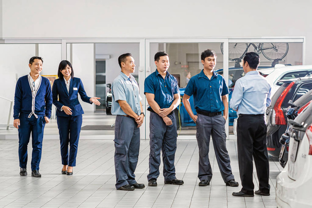 Mechanic leader Suggesting job to group of asian engineer mechanics in maintenance service center which is a part of showroom, sales representative walking and introducing the service to customer - 写真・画像