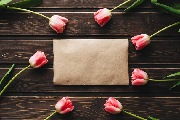 ροζ λουλούδια τουλίπες με ένα χαρτί ταχυδρομικό φάκελο σε ένα ξύλινο τραπέζι - Φωτογραφία, εικόνα