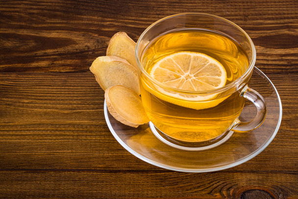 Bir bardak limonlu zencefil çayı ve ahşap bir sırtta zencefil kökü. - Fotoğraf, Görsel