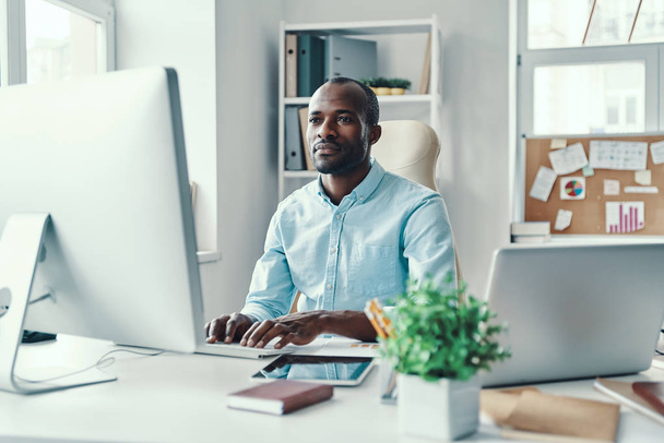 Concentrated young African man in shirt using computer while working in the office                - 写真・画像