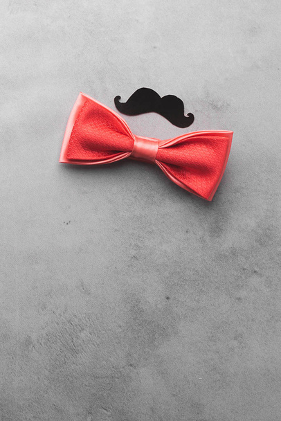 Decorative black mustache and red bow-tie on a gray background. The concept of mens holiday fathers day. Top view flat layout. Vertical frame copy space. - Fotografie, Obrázek