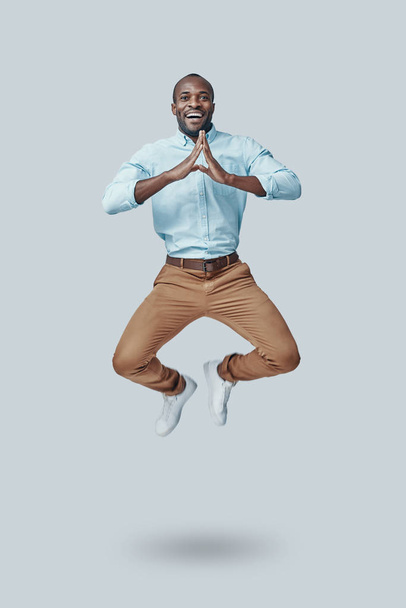 Giovane uomo africano giocoso gesticolando e gridando mentre si libra sullo sfondo grigio
 - Foto, immagini