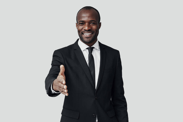 Elegant young African man in formal wear looking at camera and smiling while standing against grey background      - Foto, immagini