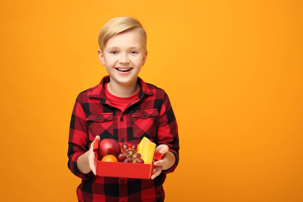 School lunch box, fruit lunch at school.Beautiful smiling caucasian boy in the red shirt on the yellow background. Horizontal, straight on. - Photo, Image