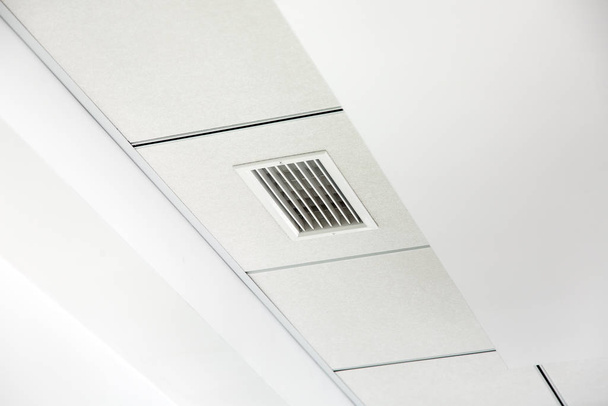 vícevrstvý bílý sádrokartonový strop a kachlový čtvercový zavěšený strop s mřížkou ventilačního systému. - Fotografie, Obrázek
