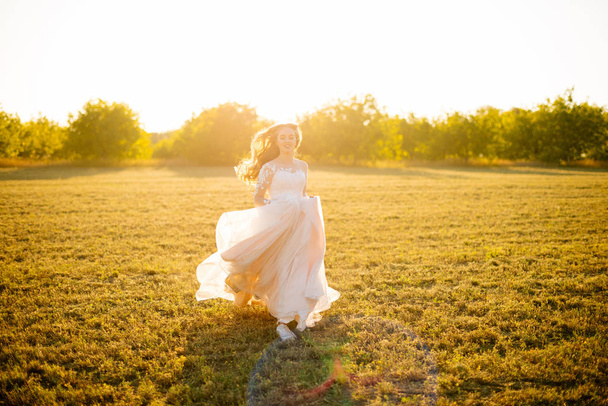 Young happy bride is running in front of the camera on the field at sunset. - Foto, Imagen
