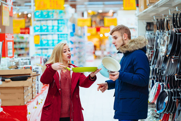 The guy and the girl choose pot and frying pan in a supermarket. - Фото, изображение
