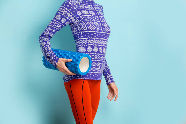  Young woman ready to do Fascia Training holding a Fascia Roll over blue background with snow print on clothes - 写真・画像