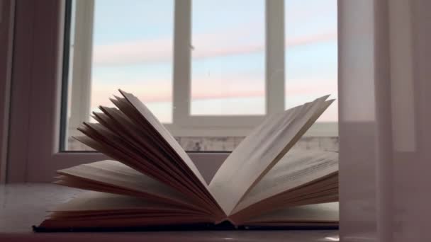 Otevřená kniha leží na parapetu, za oknem zapadá slunce, vedle ní jsou brýle na čtení. Zpomalený pohyb. - Záběry, video