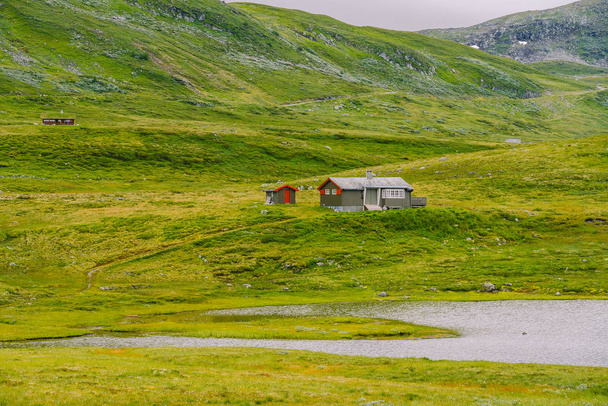 Norjalainen puuhuvila näköalalla luonnonkauniille järvelle, Norja, Skandinavia. Mökki järven rannalla maaseudulla. Turvekattoinen maja järvellä. Norjassa on tyypillinen ruoho kattohuoneisto. Tyypillinen punainen rorbu kalastusmaja
 - Valokuva, kuva