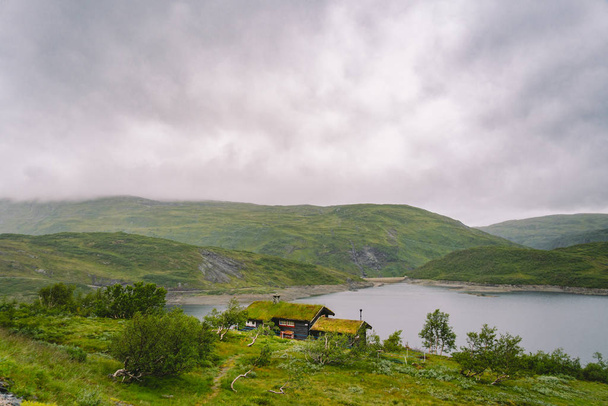 Norvég faház kilátással festői tó, Norvégia, Skandinávia. Vidéki ház a tónál. Tőzegtetős kunyhó a tónál. Tipikus fűtetős kunyhó Norvégiában. Tipikus vörös rorbu halászkunyhó - Fotó, kép
