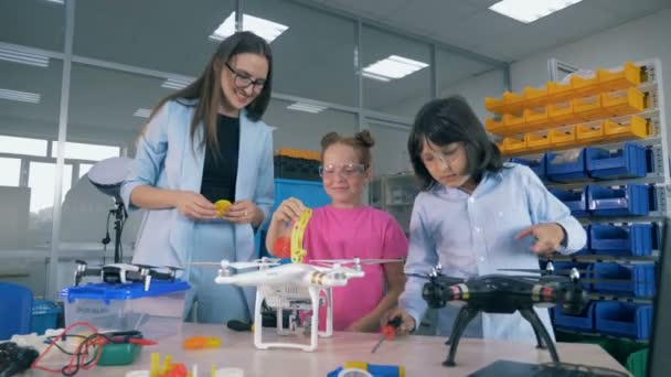 Technisches Spielzimmer mit Jugendlichen, die unter Aufsicht von Labormitarbeitern an Quadcoptern arbeiten - Filmmaterial, Video