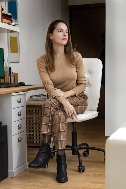 Retrato de una mujer madura de 45 a 50 años, mirando hacia otro lado pensativo, sentada en casa junto a un escritorio
. - Foto, Imagen