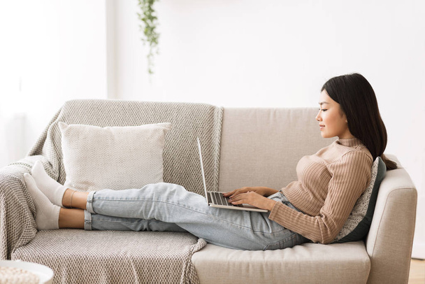 Fin de semana perezoso. Chica joven relajándose en el sofá con el ordenador portátil
 - Foto, imagen