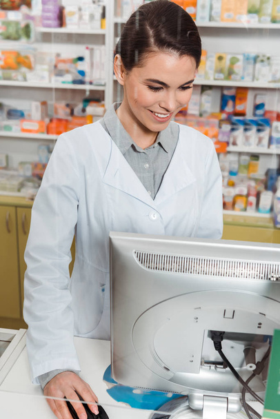 Atractivo farmacéutico sonriente utilizando el ordenador en la farmacia
 - Foto, imagen