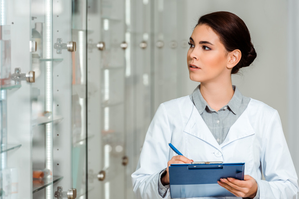 Pharmacist with clipboard looking at showcase in drugstore - Photo, Image
