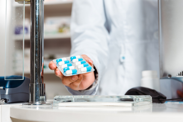 Gewassen beeld van een apotheker met blisterverpakking met pillen aan de apotheek - Foto, afbeelding