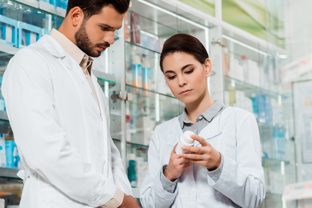 Vista a basso angolo del farmacista guardando vaso con pillole in farmacia
 - Foto, immagini