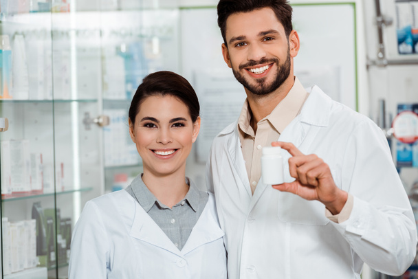 Фармацевты с банкой таблеток улыбаются перед камерой в аптеке
 - Фото, изображение