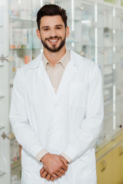 Handsome pharmacist smiling at camera by drugstore showcase - Foto, imagen